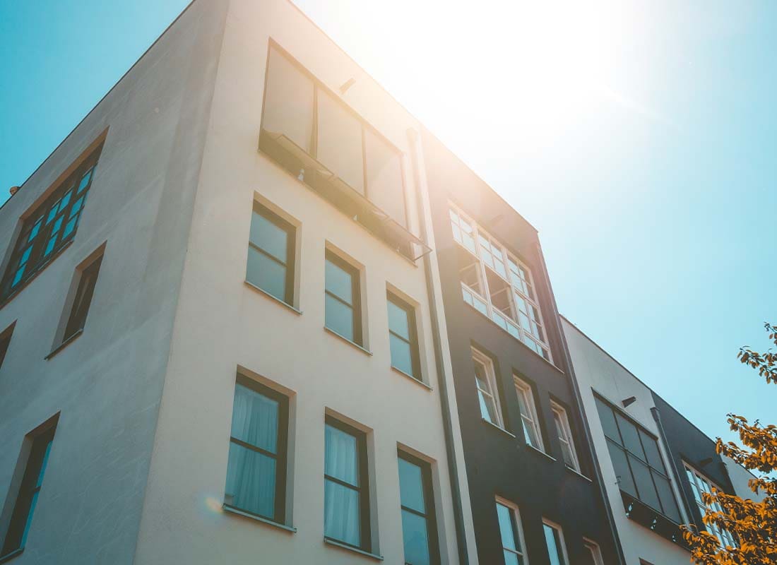 Condo Building Insurance - Angled View Looking up at a White and Black Colored Modern Condo Building with Sunlight Shining and Reflecting on Windows at Dusk