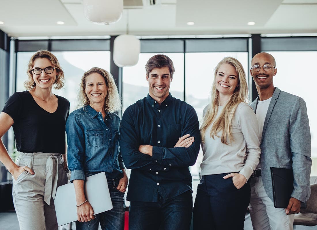 Contact - Smiling Portrait of a Successful Business Team Standing in Their Office With Lots of Light and Large Windows