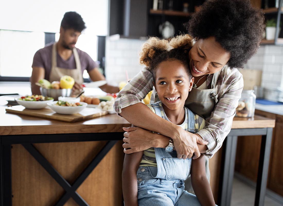 Personal Insurance - Happy Family Preparing Healthy Food in Kitchen Together While Mother Embraces Young Daughter